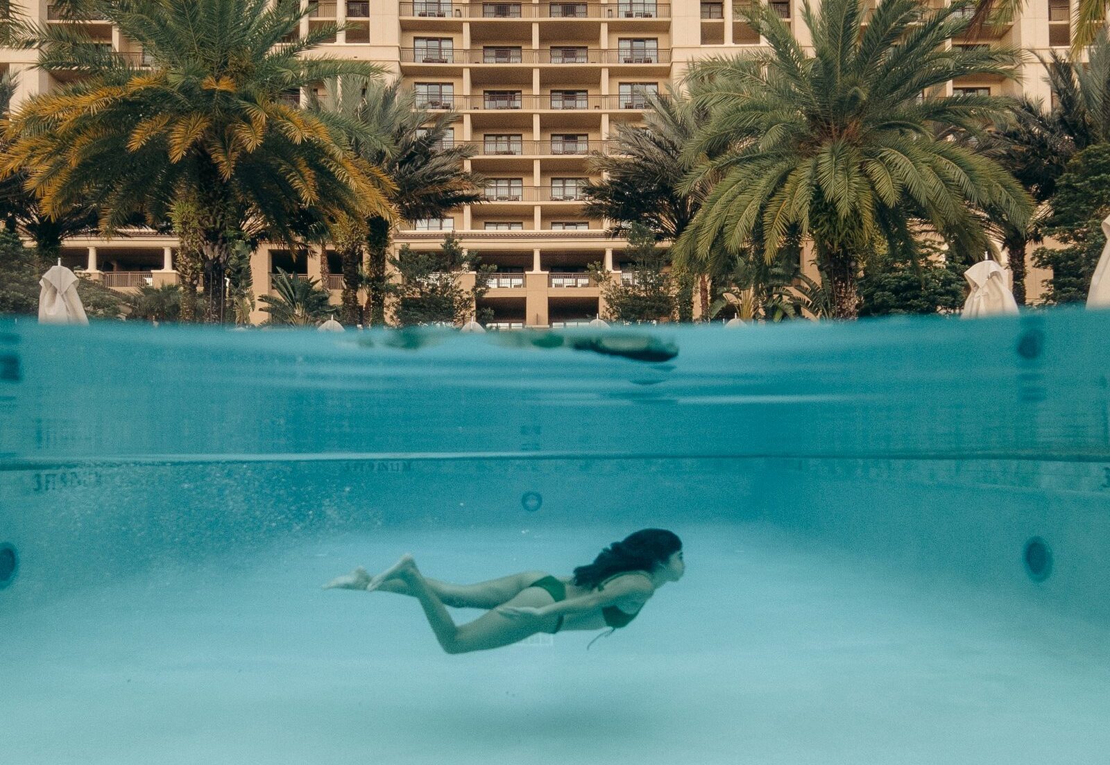 man in swimming pool near palm trees and building during daytime